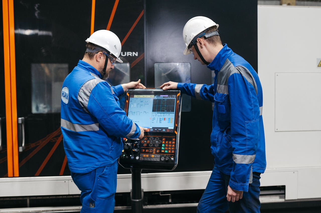Two engineers operating CNC machinery in a factory setting, wearing safety gear and uniforms.